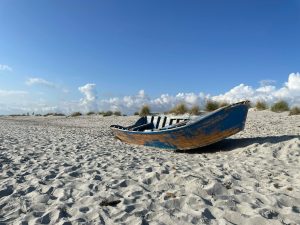 An old wooden boat rests on the sandy shores of Porto Pino, Sardegna under a clear blue sky.